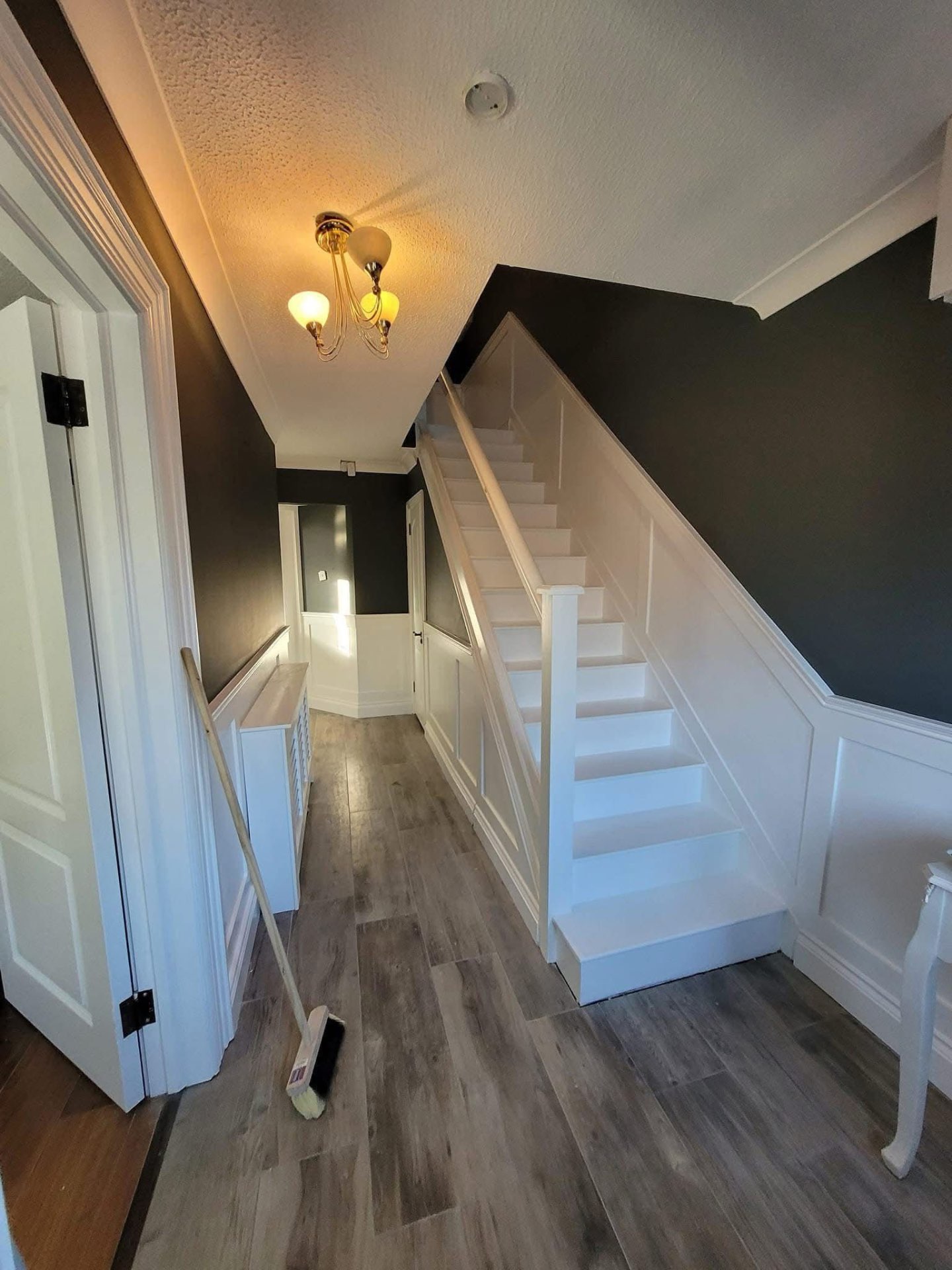 Hallway and staircase with charcoal walls, white wainscoting and freshly painted white stairs